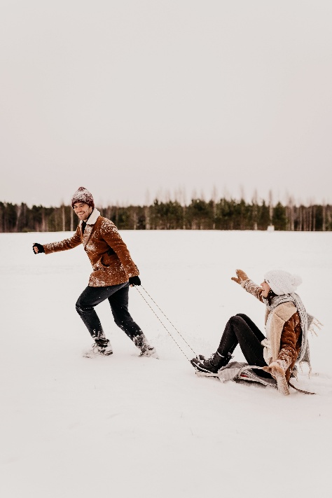 One person pulling another person on a sled across a snowy field.