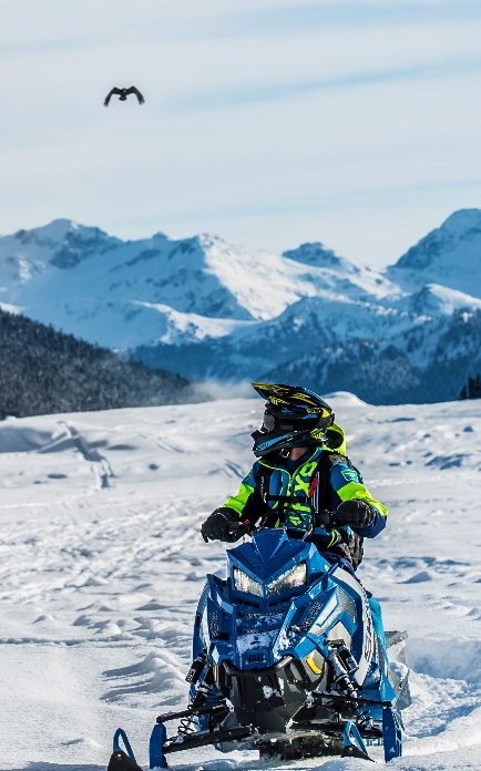A snowmobiler riding on a snowy mountain trail.